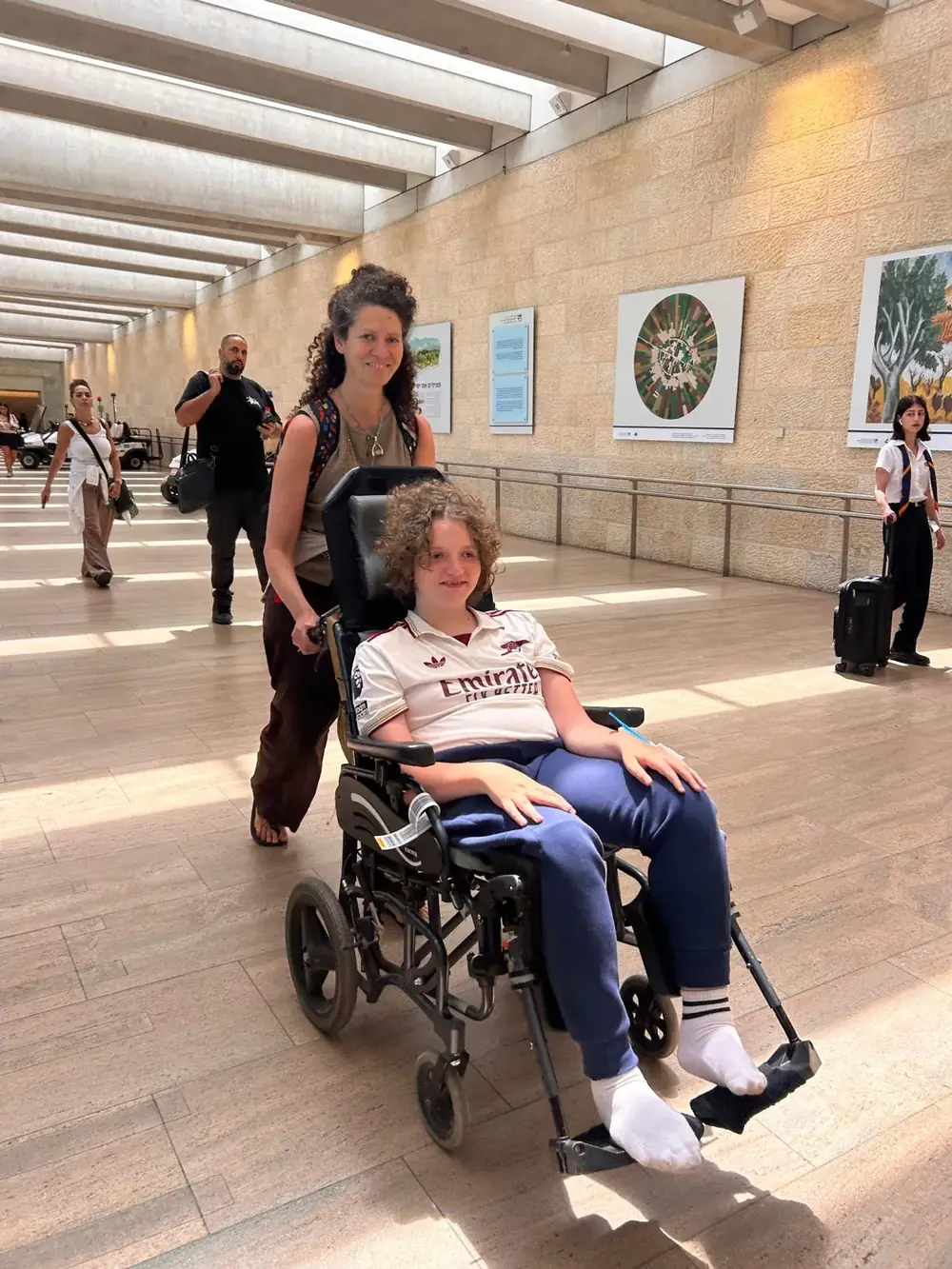 מיקאלה דוחפת את כיסא הגלגלים של אמור במסוף נתב״ג בדרך לטיפול בארה״ב